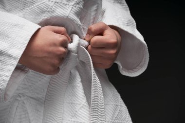 Eller yakın - dövüş sanatları kıyafeti giymiş bir genç koyu gri bir arka planda poz veriyor, bir spor konsepti