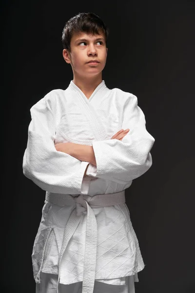 Retrato de um adolescente vestido com roupas de artes marciais posa em um fundo cinza escuro, um conceito esportivo — Fotografia de Stock