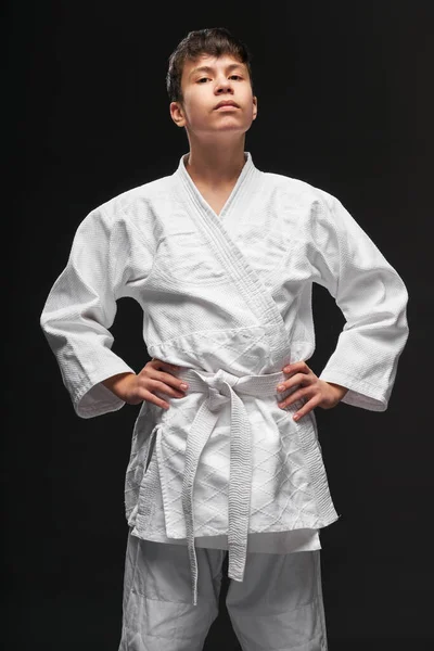 Concepto deportivo - un adolescente orgulloso vestido con ropa de artes marciales posa sobre un fondo gris oscuro, sesión de estudio — Foto de Stock