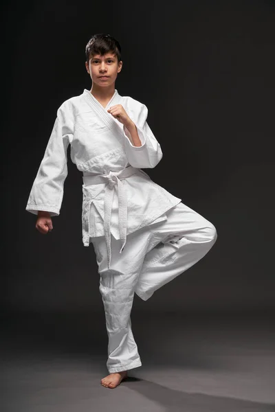 A teenager dressed in martial arts clothing poses on a dark gray background, a sports concept — 스톡 사진