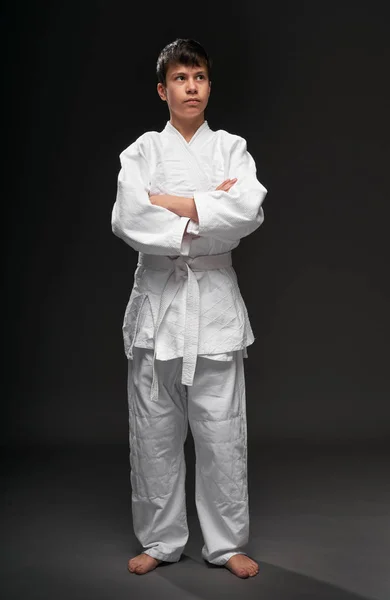 Retrato de um adolescente vestido com roupas de artes marciais posa em um fundo cinza escuro, um conceito esportivo — Fotografia de Stock