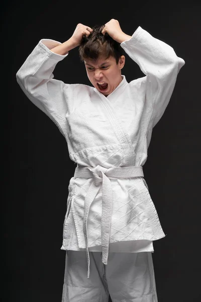 Conceito de esporte adolescente irritado vestido com roupas de artes marciais posa em um fundo cinza escuro, tiro estúdio — Fotografia de Stock