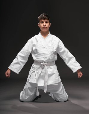 Spor konsepti - Dövüş sanatları kıyafeti giymiş bir genç koyu gri arka planda poz verir, stüdyo çekimi