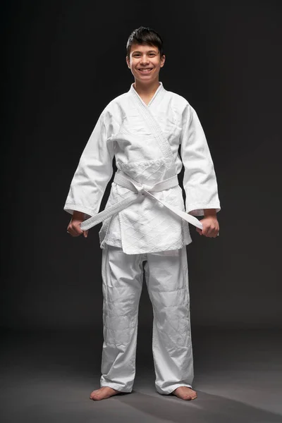 Un adolescente vestito con abiti di arti marziali posa su uno sfondo grigio scuro, un concetto sportivo — Foto Stock