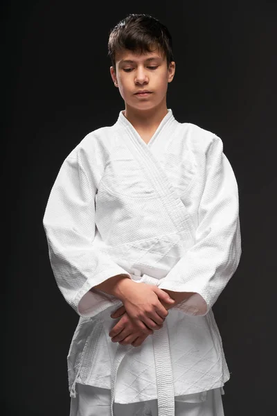 Портрет подростка, одетого в одежду боевых искусств позирует на темно-сером фоне, спортивная концепция — стоковое фото