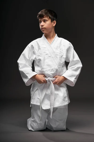 Sport concept - een tiener gekleed in vechtsport kleding poseert op een donkergrijze achtergrond, studio shoot — Stockfoto