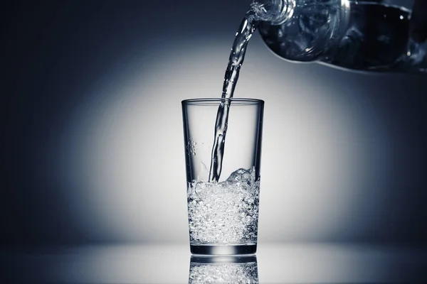 Csillogó vizet öntök egy pohárba sötétkék alapon. — Stock Fotó