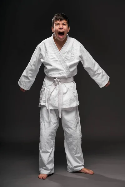 Een tiener gekleed in vechtsport kleding poseren en huilen op een donkergrijze achtergrond, een sport concept — Stockfoto