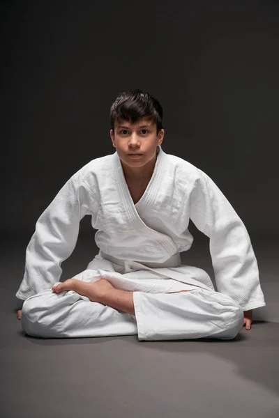 Un adolescente vestido con ropa de artes marciales posa sobre un fondo gris oscuro, un concepto deportivo — Foto de Stock