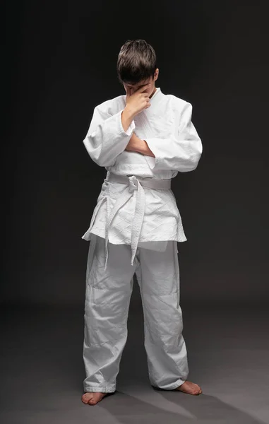 Smutny nastolatek ubrany w odzież sztuk walki mający problem na ciemnym szarym tle, koncepcja sportowa — Zdjęcie stockowe