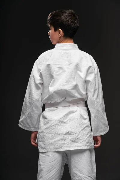 Visão traseira de um adolescente vestido com roupas de artes marciais posa em um fundo cinza escuro, um conceito de esportes — Fotografia de Stock