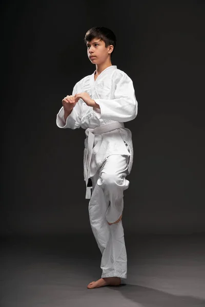 Um adolescente vestido com roupas de artes marciais posa em um fundo cinza escuro, um conceito esportivo — Fotografia de Stock