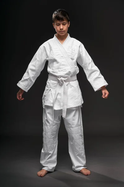 Retrato de un adolescente vestido con ropa de artes marciales posa sobre un fondo gris oscuro, un concepto deportivo — Foto de Stock