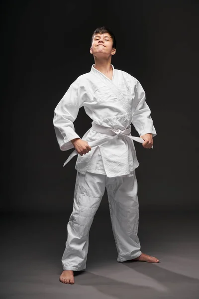 Un adolescente vestido con ropa de artes marciales posa sobre un fondo gris oscuro, un concepto deportivo — Foto de Stock