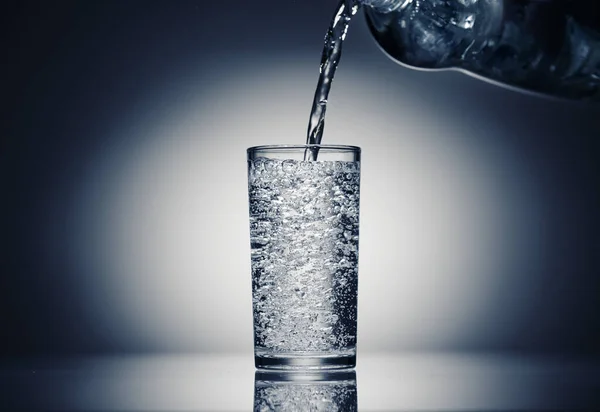 Verser de l'eau pétillante dans un verre sur un fond bleu foncé — Photo