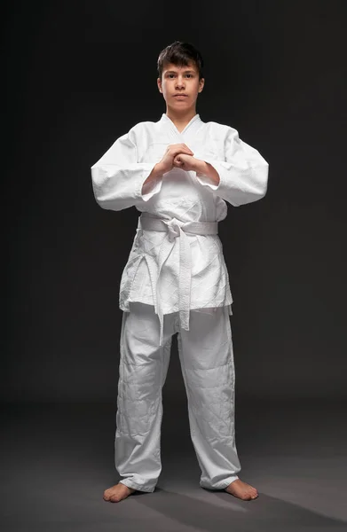 Retrato de un adolescente vestido con ropa de artes marciales posa sobre un fondo gris oscuro, un concepto deportivo —  Fotos de Stock