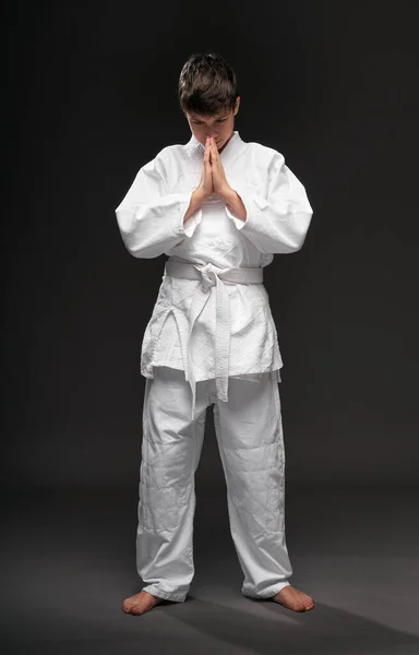 Retrato de um adolescente vestido com roupas de artes marciais posa em um fundo cinza escuro, um conceito esportivo — Fotografia de Stock