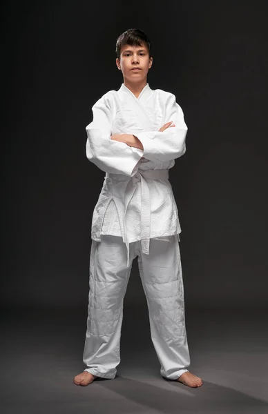 Портрет подростка, одетого в одежду боевых искусств позирует на темно-сером фоне, спортивная концепция — стоковое фото