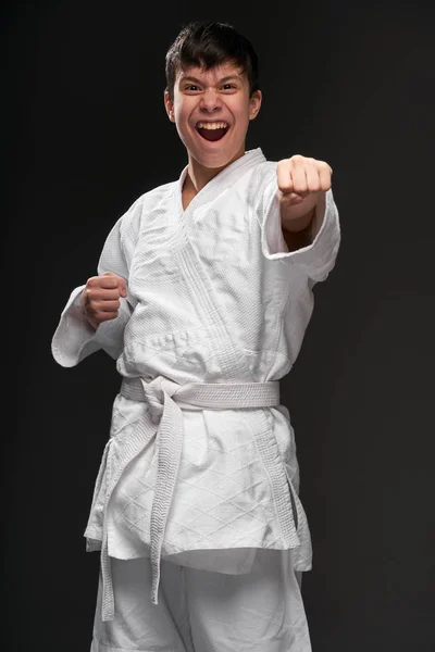 Um adolescente vestido com roupas de artes marciais posando e chorando em um fundo cinza escuro, um conceito esportivo — Fotografia de Stock