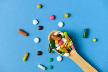Hap, tablet, vitamin, ilaç, omega 3 balık yağı, jel kapsülleri, ilaç ve sağlık hizmetleri için gıda takviyesi dolu tahta kaşık. Mavi arkaplan.