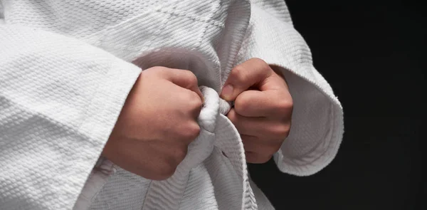 Mani primo piano adolescente vestito in abbigliamento arti marziali in posa su uno sfondo grigio scuro, un concetto di sport — Foto Stock