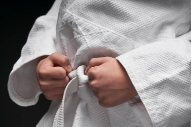 Eller yakın - dövüş sanatları kıyafeti giymiş bir genç koyu gri bir arka planda poz veriyor, bir spor konsepti