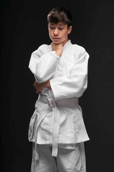 A teenager dressed in martial arts clothing poses on a dark gray background, a sports concept — Stock Photo, Image