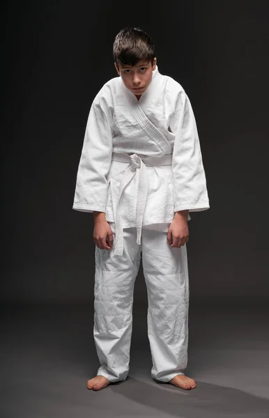 Adolescente infeliz vestido con ropa de artes marciales posa sobre un fondo gris oscuro, con depresión, concepto deportivo — Foto de Stock