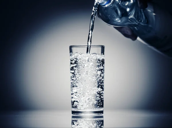 Menuangkan air berkilau dalam gelas dengan latar belakang biru tua — Stok Foto