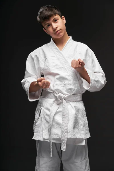 Conceito de esporte - um adolescente vestido com roupas de artes marciais posa em um fundo cinza escuro, tiro estúdio — Fotografia de Stock