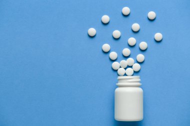 Beyaz ilaç hapları, haplar, kapsüller patlar ya da mavi arka plandaki şişeden fışkırır. Metin için boşluk kopyala - ilaç tedavisi kavramı, sağlık hizmetleri