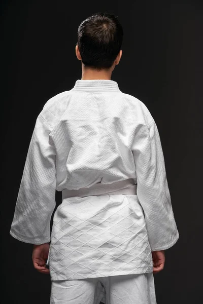Вид збоку підлітка, одягнений у бойові мистецтва одяг позує на темно-сірому тлі, спортивна концепція — стокове фото