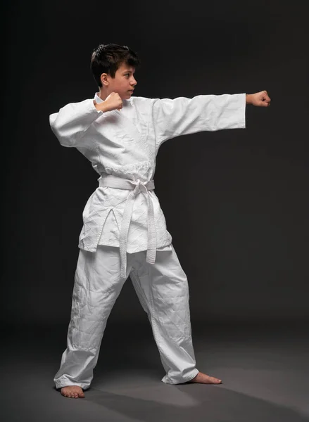 A teenager dressed in martial arts clothing poses on a dark gray background, a sports concept — 스톡 사진