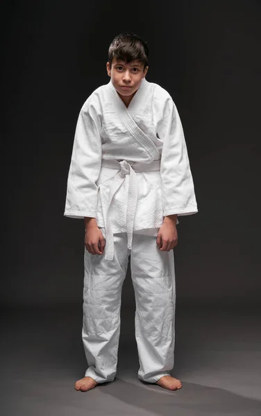 Un adolescente vestido con ropa de artes marciales posa sobre un fondo gris oscuro, con depresión, concepto deportivo — Foto de Stock