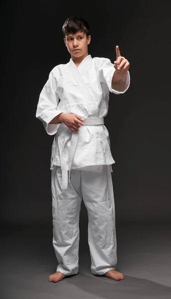 暗い灰色の背景にポーズをとってジェスチャーする武道の服を着た10代の若者スポーツの概念 — ストック写真
