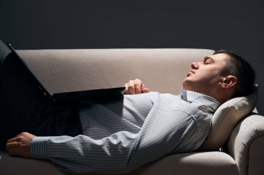 İş adamı kanepede dizüstü bilgisayarla yatıyor ve dinleniyor.