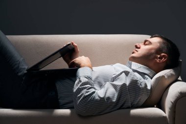 İş adamı kanepede dizüstü bilgisayarla yatıyor ve dinleniyor.
