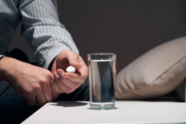 Çok çalışan bir iş adamı kanepede oturup ilaç alıyor. Yanında haplar ve bir bardak su vardı..
