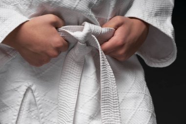 Dövüş sanatları kıyafeti giymiş genç bir sporcunun elleri, koyu gri bir arka planda, bir spor konseptinde poz verir.