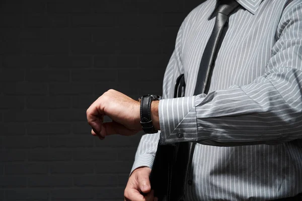 Businessman closeup portrait, he stands and looks at his wrist watch, dark wall background