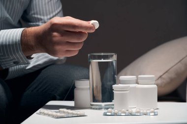 Çok çalışan bir iş adamı kanepede oturup ilaç alıyor. Yanında haplar ve bir bardak su vardı..