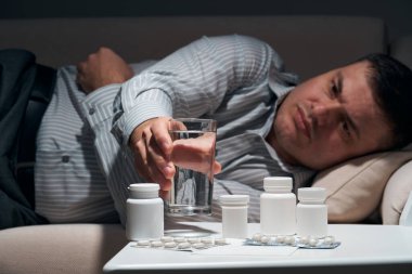 Çok çalışan iş adamı kanepede uzanıyor ve dinleniyor. Yanında haplar ve bir bardak su vardı..