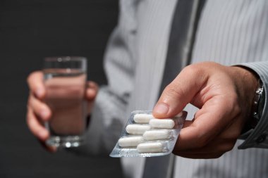 İş adamı yakın plan portresi, ayakta duruyor ve haplarla poz veriyor, sağlık ve ilaç konsepti, karanlık duvar arkaplanı