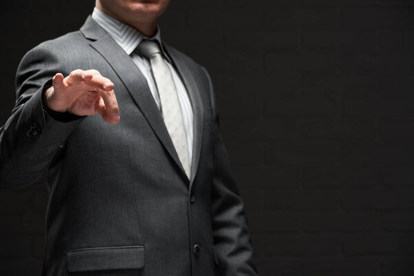 бизнесмен демонстрирует что-то в пальцах, одетый в серый костюм, темный фон стены

