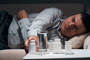 Çok çalışan iş adamı kanepede uzanıyor ve dinleniyor. Yanında haplar ve bir bardak su vardı..