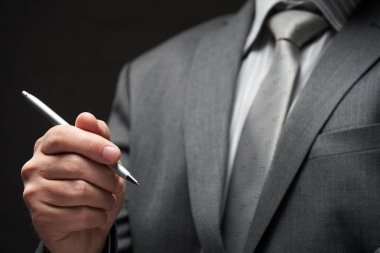 Bir kalem yakın plan iş adamı eli, gri takım elbise, koyu duvar arkaplan