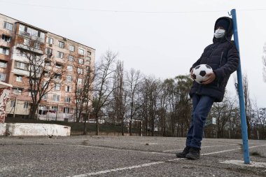 Salgın ve karantina kavramı. Yüzü maskeli bir çocuk ve şehirde tek başına bir top.