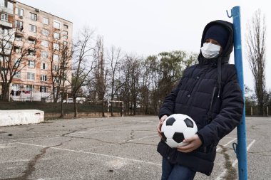 Salgın ve karantina kavramı. Yüzü maskeli bir çocuk ve şehirde tek başına bir top.