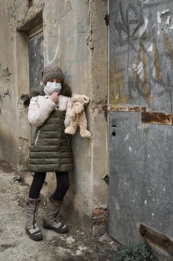Salgın ve karantina kavramı. Yüz maskesi takmış bir kız ve şehirde tek başına bir oyuncak.