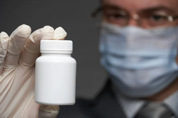 a man with a mask on his face for antivirus individual protection shows a white blank bottle for medicine, pills - healthcare and medicine concept, prevention tips